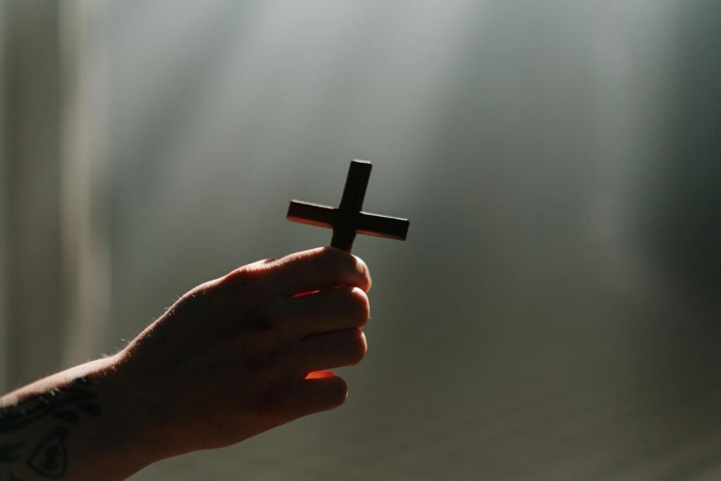 A hand holds a cross in a beam of light, symbolizing faith and spirituality.