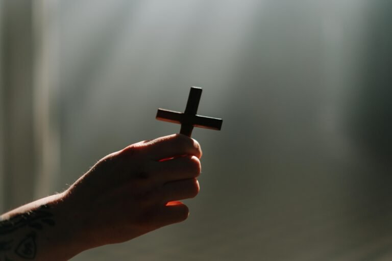 A hand holds a cross in a beam of light, symbolizing faith and spirituality.